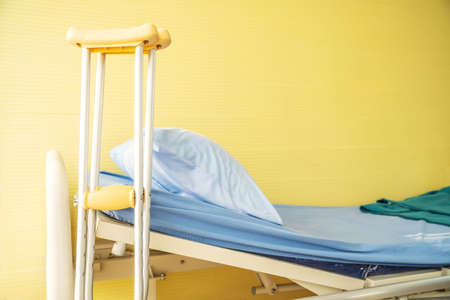 Empty bed with pillow and blanket and intravenous (IV) stand and walking stick, Walking stick cane used by disable patient for balancing, Healthcare,medical insurance and Physical therapy concept.の写真素材
