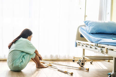 Patient asian woman wear a sick suit feeling unwell and worry sitting and holding knees in hospital room floor near patient bed, Concept of healthcare patient lifestyle and medical.の写真素材