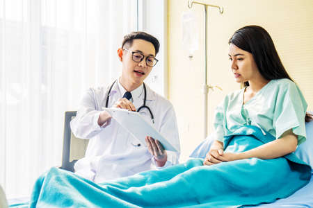 Male doctor talking to Female patient in hospital bed, while pointing notes on clipboard, Medicine and health care concept, selective focus pointの写真素材