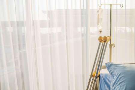 Empty bed with pillow and blanket and intravenous (IV) stand and walking stick, Walking stick cane used by disable patient for balancing, Healthcare,medical insurance and Physical therapy concept.の写真素材