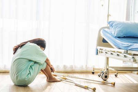 Patient asian woman wear a sick suit feeling unwell and worry sitting and holding knees in hospital room floor near patient bed, Concept of healthcare patient lifestyle and medical.の写真素材