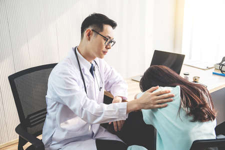 Friendly male doctor consoling female patient and use your hand to shoulder to help her relax in office during reception, The concept of counseling and health care.の写真素材
