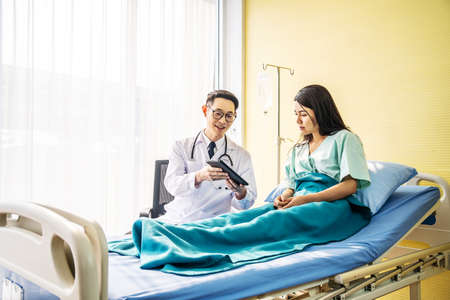 Asian male doctor talking to asian female patient in bed, while explaining exam results in computer to patient at medical consultation, Medicine and health care concept, selective focus pointの写真素材