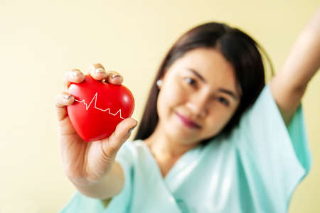 Portrait of young woman patient shows a red heart on the hand and sitting bed with smiles and bright facial expressions, Have better symptoms in the patientâs wardの写真素材