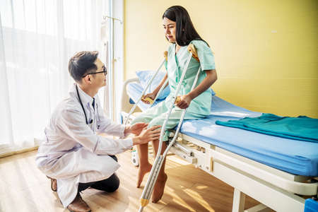 Asian male Doctor or Physiotherapist examining knee, female patient with injured leg or knee after accident and explain to her the diagnosis of problem in clinic, Sport exercise injuries.の写真素材