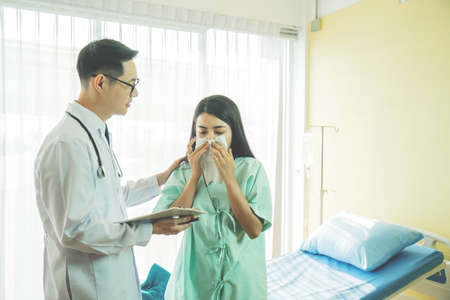 Primary care doctor making diagnosis to sick woman, unhappy patient using a tissue to sneeze and blowing her nose and get high fever from flu and cold, Patient care and healthcare.の写真素材