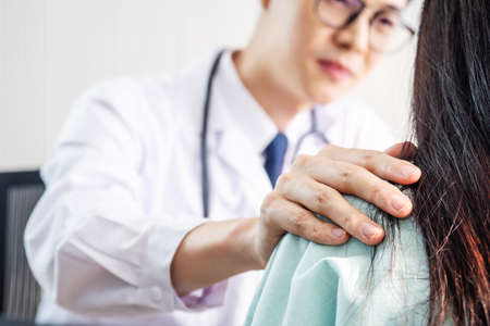 Friendly male doctor talk with thankful female patient and hold patient shoulder in office during reception, Welcoming friend trust physical healthy lifestyle exam interview conceptの写真素材