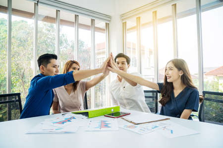 Asian Business people team with casual suit standing and giving high five at office, happy action for teamwork in the modern workplace, employees group celebrate corporate success togetherの写真素材