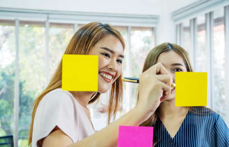Asian creative business women are writing note on the text sheet after thinking new idea and planning project with colleague ,Group of employee brainstorming idea on glass wall and stickyの写真素材