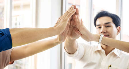 Asian Business people team with casual suit standing and giving high five at office, happy action for teamwork in the modern workplace, employees group celebrate corporate success togetherの写真素材