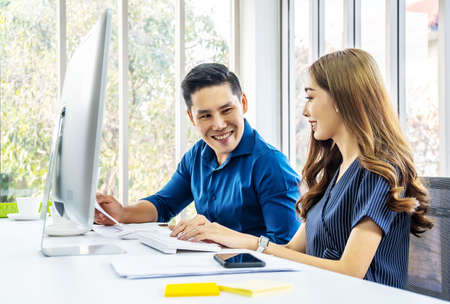 Image of two young business woman and man discussing questions while using computer at workplace in modern office. Teamwork, meeting and brainstorming conceptの写真素材