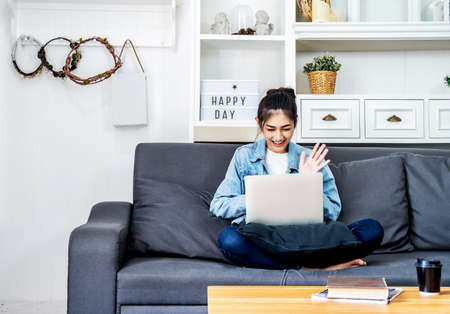 Asian teenage girl is sitting on the sofa in her own house talking with her colleagues to a project work on a computer about her job at the companyの写真素材