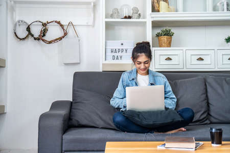 Asian teenage girl is sitting on the sofa in her own house talking with her colleagues to a project work on a computer about her job at the companyの写真素材