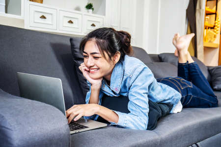 Asian woman is resting on the sofa in her own house, chatting on a video call with a close female...