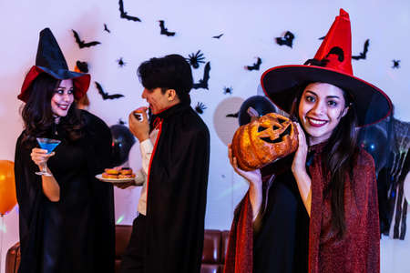 Young Asian woman in costume celebrating Halloween holding a carved pumpkin. Celebration of Group...