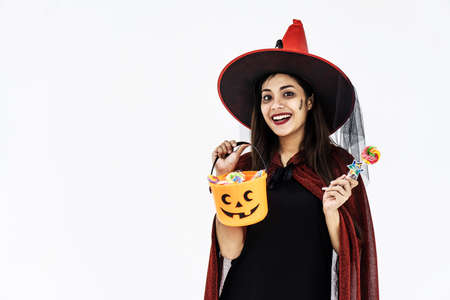 Halloween Party girl. Beautiful young woman in witches hat and short dress holding tank orange and...