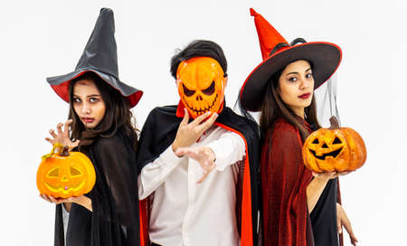 Three young people dressed in different costumes holding pumpkin for Halloween, isolated on white backgroundの写真素材