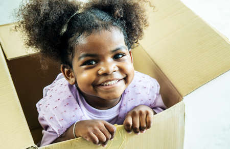 Happy cute active little african american kids girl play riding in cardboard boxes feel excited to move in new house, playful overjoyed black sister have funの写真素材