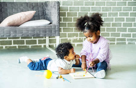 Cute black african american little girl and boy drawing book on floor indoors,  African people - Childrenの写真素材