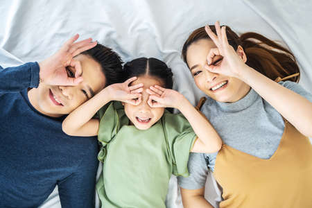 Close up photo of happy asian family lying on floor making binoculars with their hands and looking at cameraの写真素材