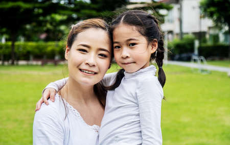 Cute asian mother and daughter smiling and hugging in love playing in the parkの写真素材