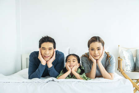 Happy young family having fun in the morning in bed together and looking at cameraの写真素材
