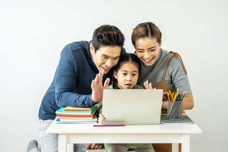Happy young mother and father and little daughter making video call with laptop computer, gesturing hi, having conversation with  grandfather or grandma using wireless internet connectionの写真素材