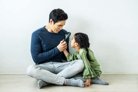 Happy father playing magnifying glass with a daughter in homeの写真素材