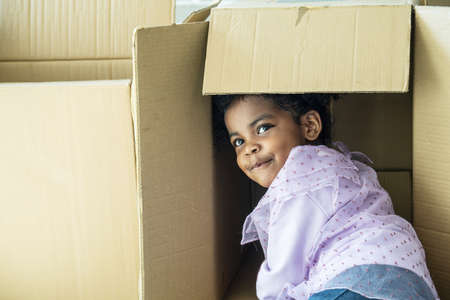 Relocating delivery services. Delivering happiness, African american cute baby girl enjoy playing with cardboard box at home, Insurance post package. Deliver your treasures. Storage for toys.の写真素材