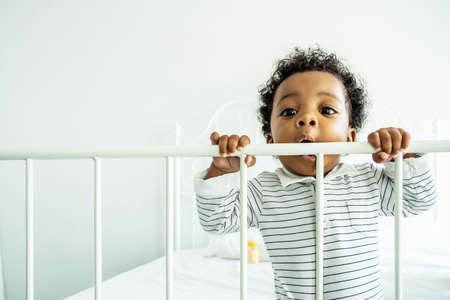 African American child boy stand near bed rail play and he look happy and innocent. Concept of happiness emotion occur with good health and support from family.の写真素材