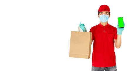 Delivery man employee in red cap t-shirt uniform mask gloves hold craft paper packet with food and phone isolated on white background, Service quarantine pandemic coronavirus virus flu conceptの写真素材