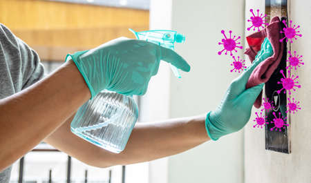 A moving hand of man disinfecting lift push button by spraying sanitizer bottle and using fabric wet wipe cleaning. Protection against infectious virus, bacteria and germs, Coronavirus, Covid-19の写真素材