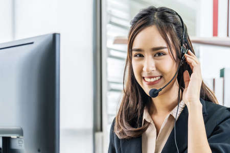 Smiling friendly asian female call-center agent with headset working on support hotline in the officeの写真素材