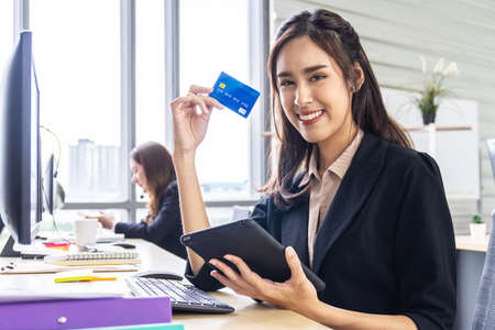 internet banking, online shopping and technology concept, happy smiling asian woman using tablet and credit card to shop online at officeの写真素材