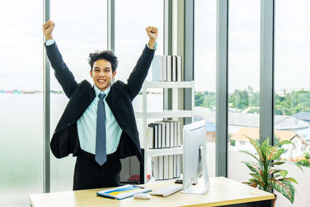 Cheerful BusinessMan Celebrating Success in office, employee got promoted or having great opportunity, applicant received job concept,arms outstretchedの写真素材