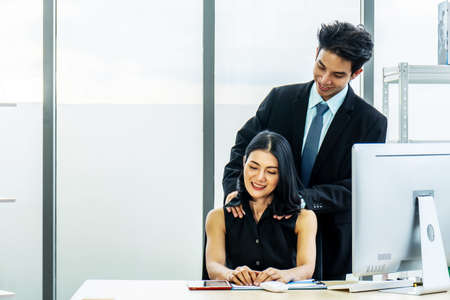 Exhausted businesswoman sitting at desk typing on laptop while are being massaged at shoulder by businessmen in their officesの写真素材