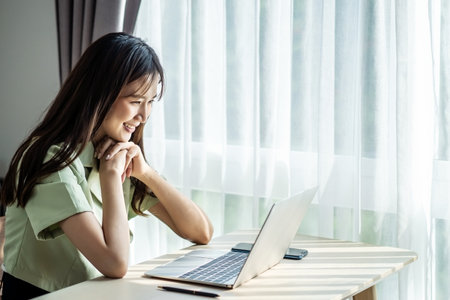 Smiling young asian woman using laptop in home, beautiful girl shopping or chatting online in social network, having fun, watching movie, freelancer working on computer projectの写真素材