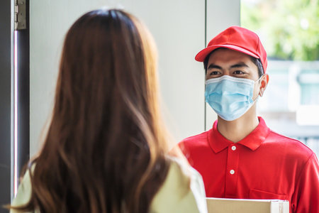 Delivery man in red uniform holdinging parcel boxes to a woman customer - courier service conceptの写真素材