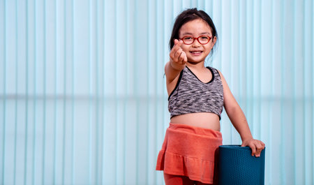 Girl child holding yoga mat at home and thumbs up. meditation center background. Exercise mat rolling keeping after.の写真素材