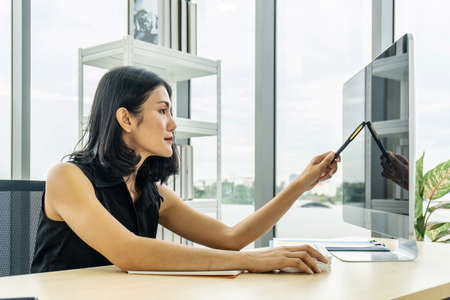 Portrait of asian business woman pointing with pen and thinking over a subject while sitting in...