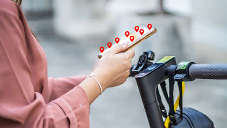 Close up of hand woman in holding smartphone hands and using maps app before riding by electric scooter in the cityの写真素材
