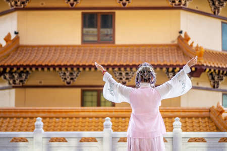 Back side of cheerful beautiful asian chinese girl wearing traditional Chinese dress with hands up in the chinese templeの写真素材