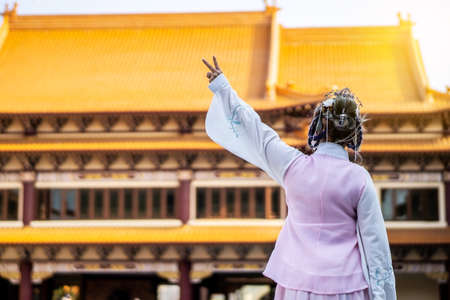 Back side of beautiful asian chinese girl wearing traditional Chinese dress showing fingers doing victory sign in the Chinese templeの写真素材