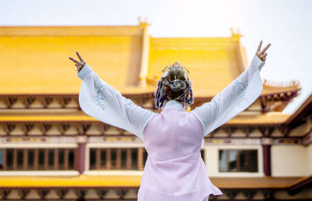 Back side of beautiful asian chinese girl wearing traditional Chinese dress showing fingers doing victory sign in the Chinese templeの写真素材