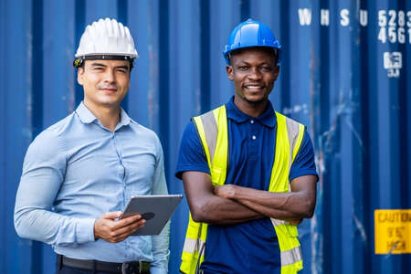 Confident port manager and engineer while stand crossed arms and smiling at freight containersの写真素材