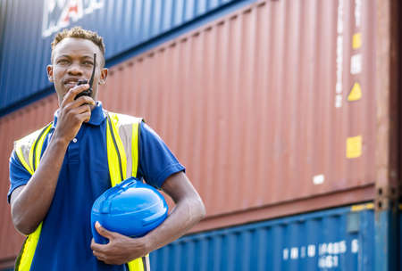 Adult African american men worker Check and control loading freight Containers by use radio at commercial shipping dock feeling curious. Cargo freight ship for import export conceptの写真素材