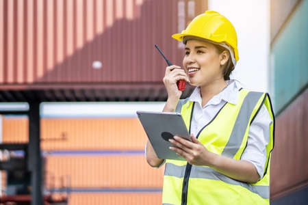 Young asian female engineer or manager holding a Tablet and use of radio communication to control container load in industrial transport and logistics conceptsの写真素材