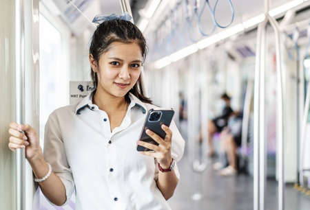 Young Asian woman passenger standing and using cell phone inside empty subway or sky train car, leisure and daily lifeの写真素材