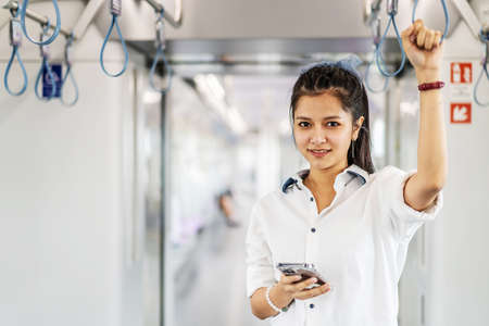 Young Asian woman passenger standing and using cell phone inside empty subway or sky train car, leisure and daily lifeの写真素材