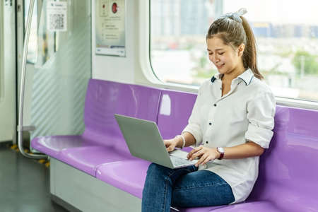 Beautiful asian woman working urgently on a laptop computer at the electric train in the morningの写真素材